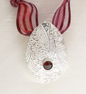 Textured pendant with garnet, hung on ribbon